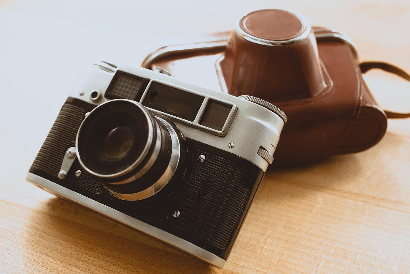 an old fashioned camera sits next to a brown leather case