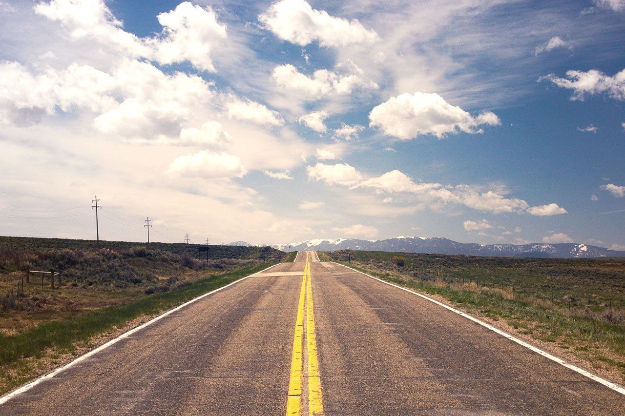 A road with a yellow line on the middle of it going through a field.