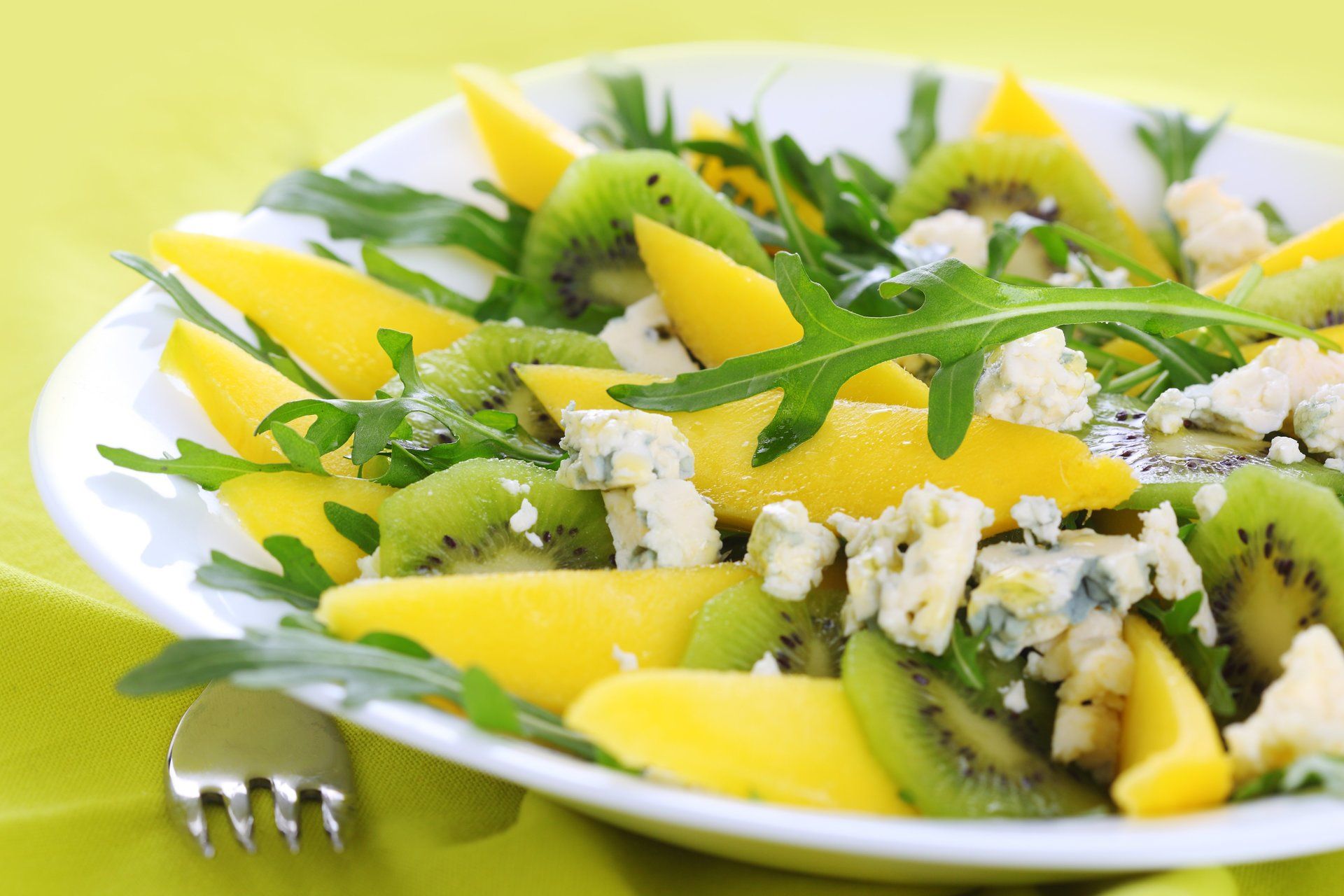 un plato blanco cubierto con una ensalada de kiwi, mango y queso