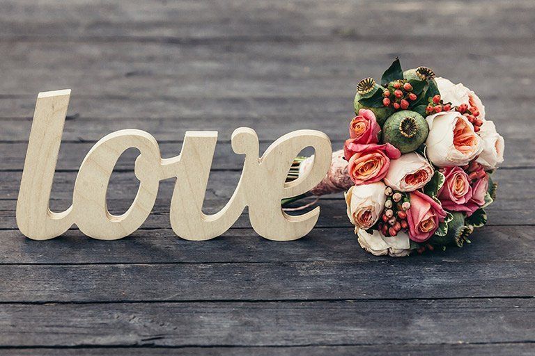 A wooden sign that says `` love '' next to a bouquet of flowers on a wooden table.