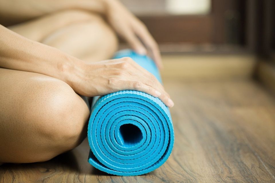 A women sitting cross legged with a light blue yoga mat rolled up in front
