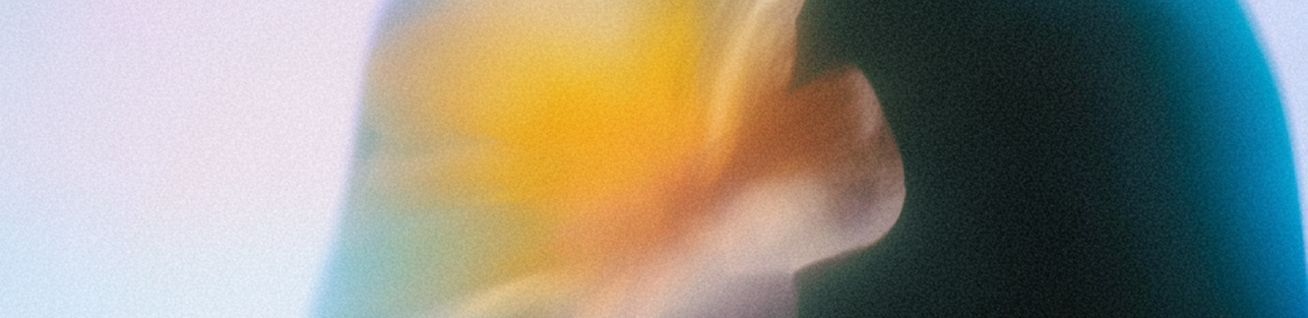 Blurred close-up of a person’s hand against a teal background with warm orange and white light.