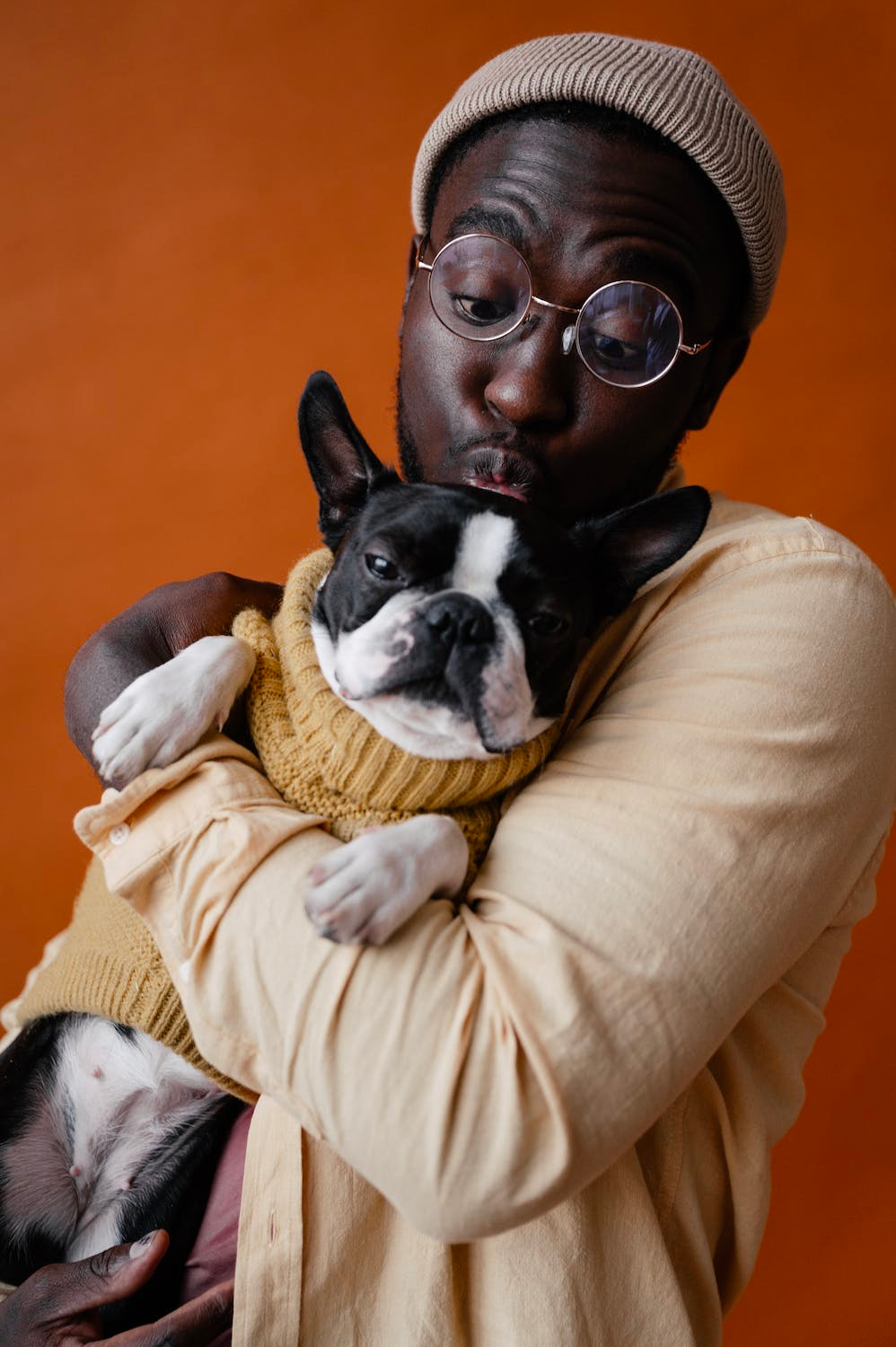 A man is holding a dog in his arms and the dog is wearing a sweater.