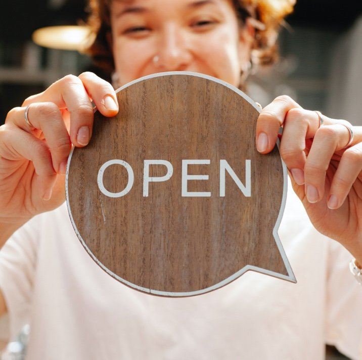A woman is holding a wooden sign that says open