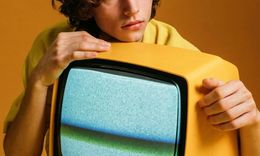 Man resting chin on a yellow, static-filled television. Yellow background.
