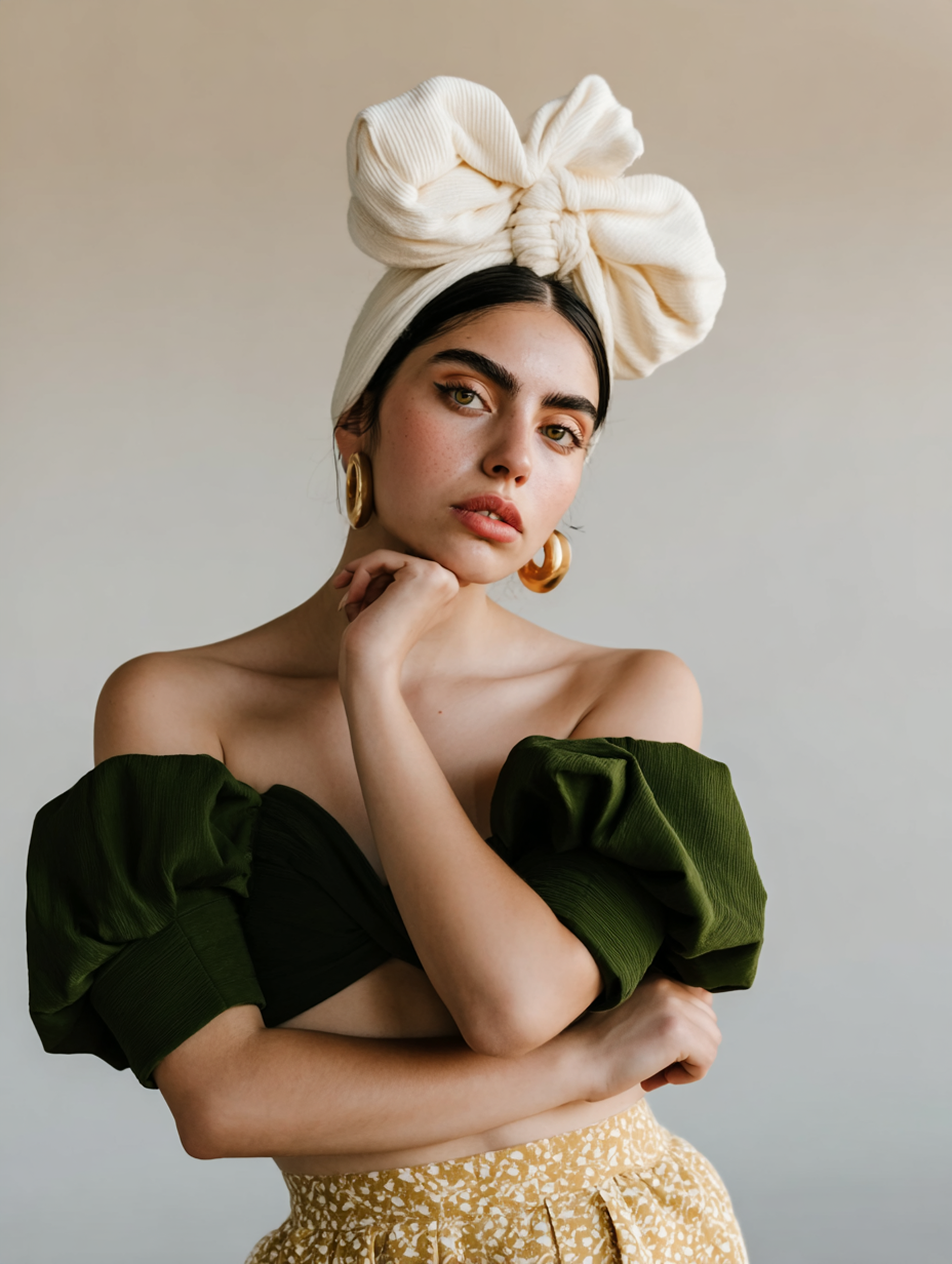Portrait of a model in a cream head wrap, green off-shoulder top, and gold skirt, posing against a neutral background