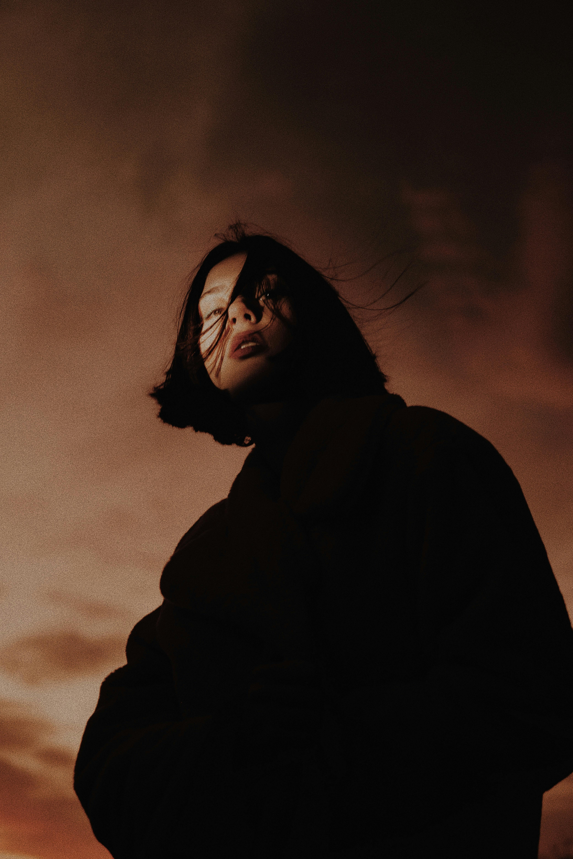 Silhouette einer Person mit kurzen Haaren, die nach oben blickt, vor einem orange-braunen Himmel.