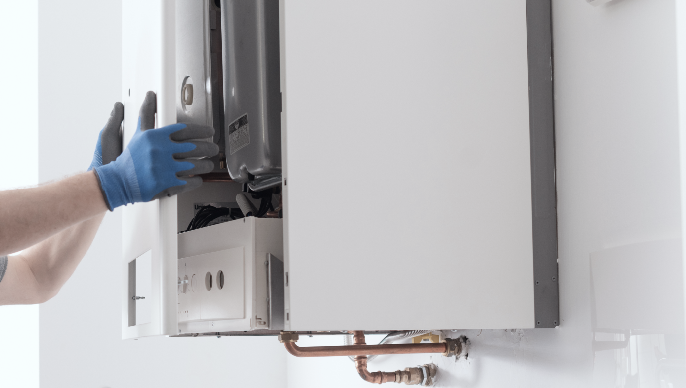 Person in blue gloves working on a white wall-mounted boiler. Copper pipes visible.