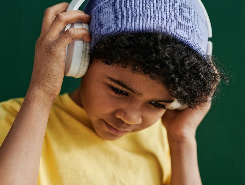 A young boy wearing headphones and a purple hat.