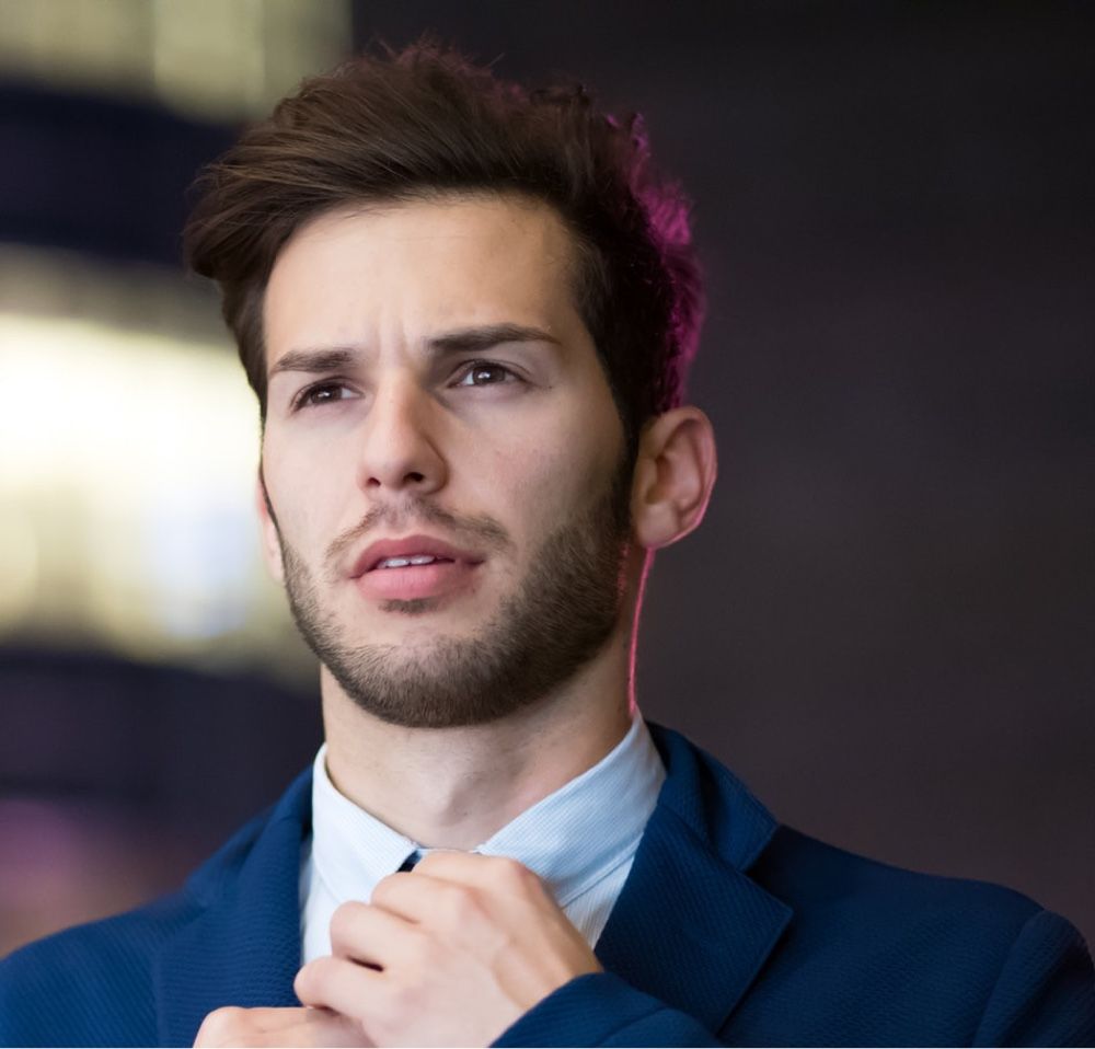 A man in a blue suit is adjusting his tie