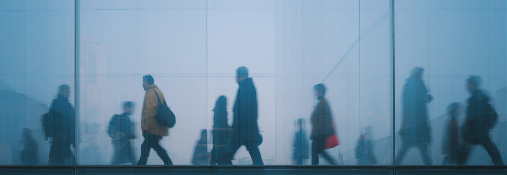 Silhouetted commuters walking through a foggy blue-lit train station hallway
