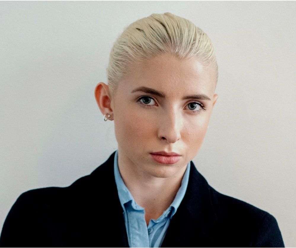 A woman with blonde hair is wearing a blue shirt and a black jacket