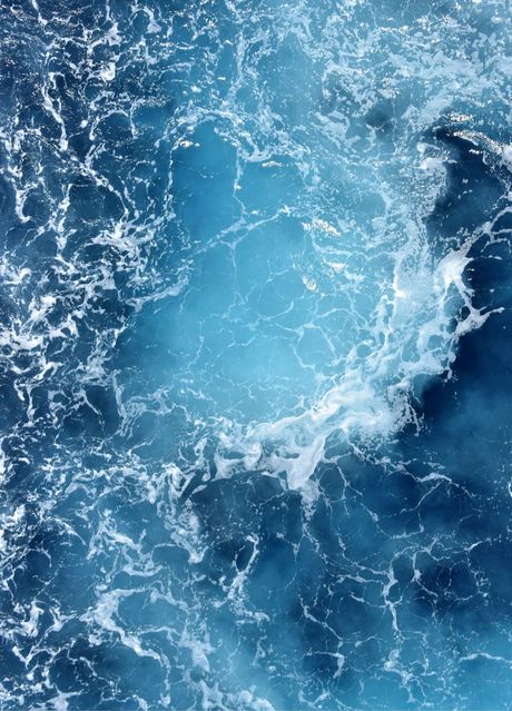 Vibrant blue ocean water with white foamy waves and swirls.