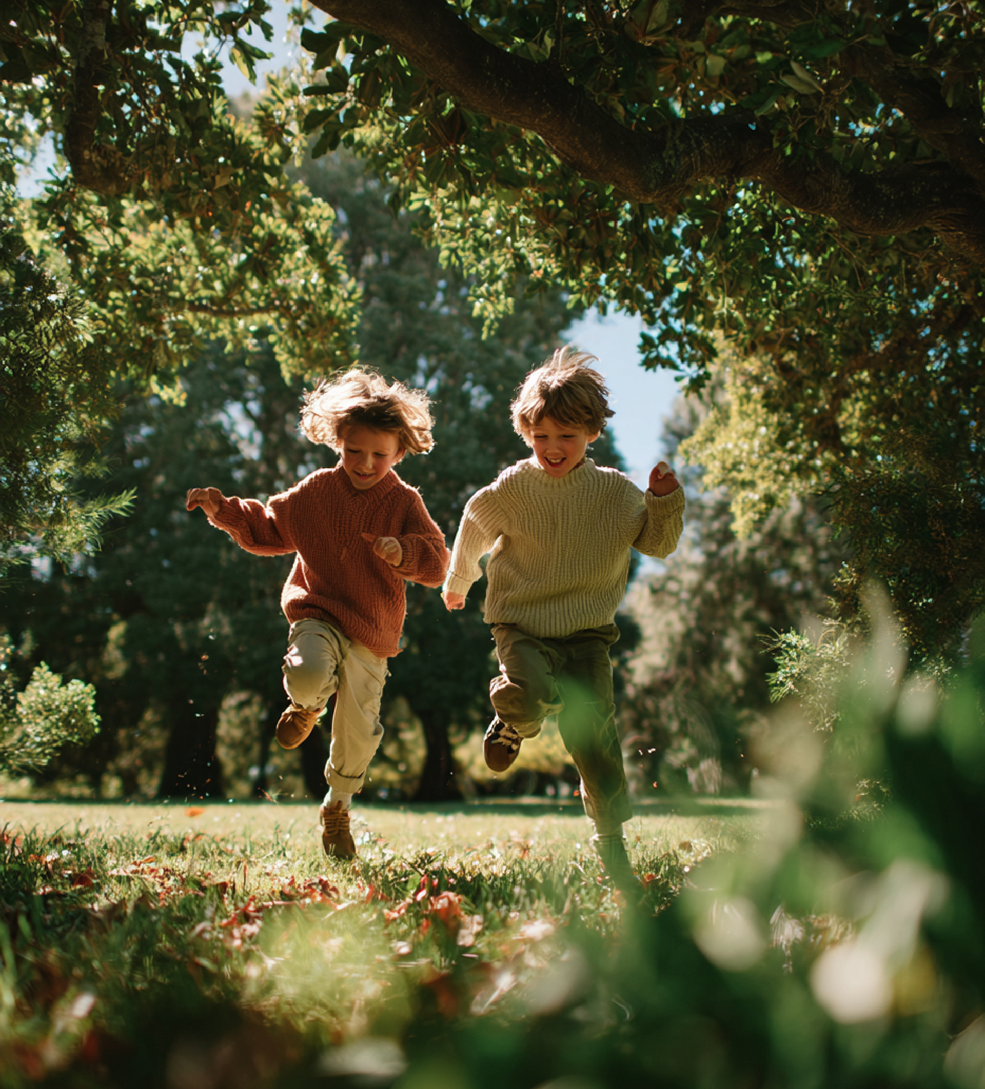 Two children running in a park, under a large tree. Green grass and foliage.