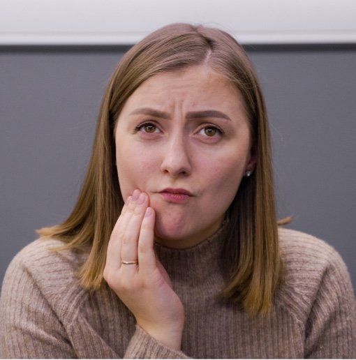 Woman with a pained expression holds her hand to her jaw, suggesting tooth pain.