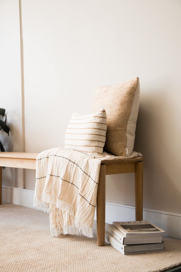 Wooden bench with striped and beige pillows, draped blanket, and stacked books against a light wall