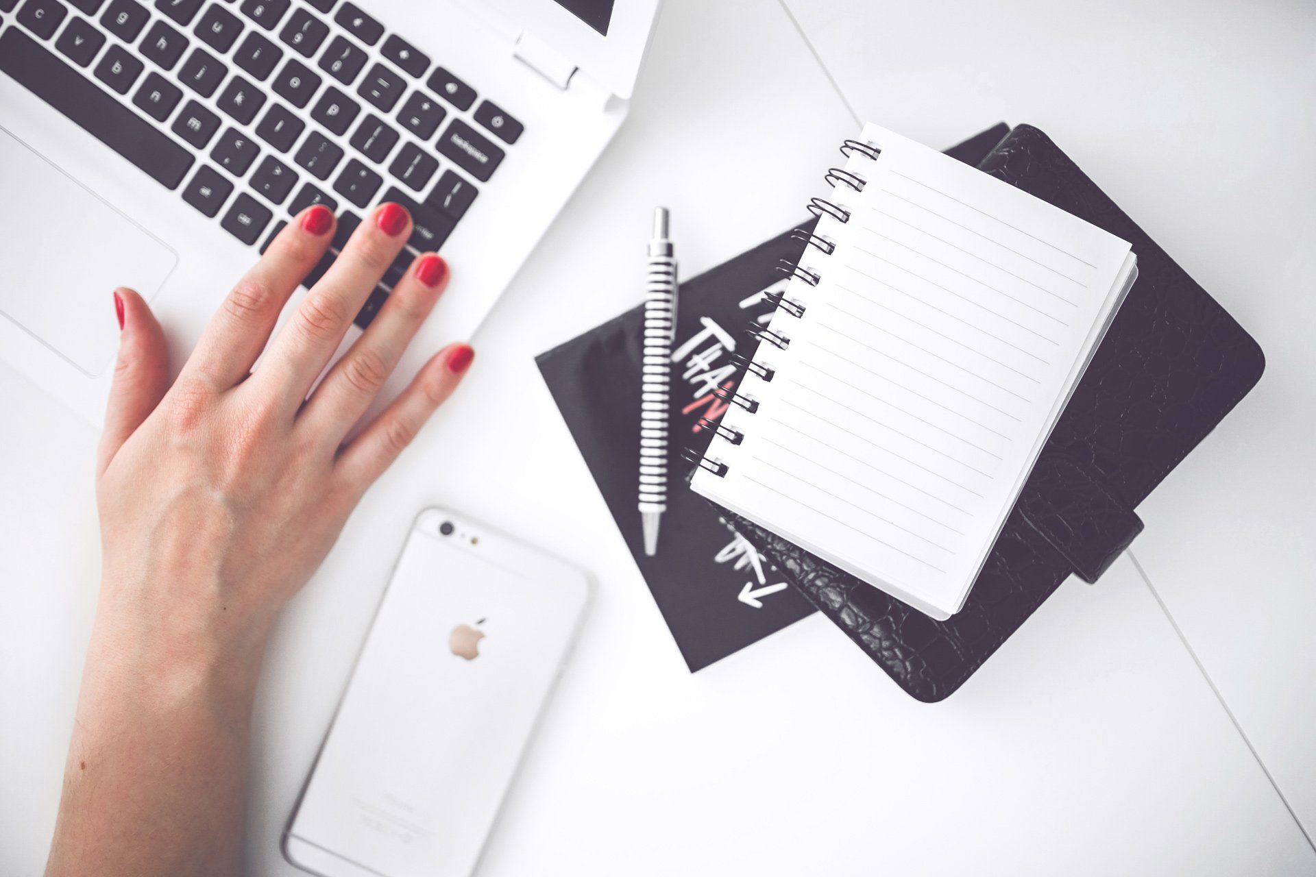 A woman is typing on a laptop next to a notebook and a cell phone.