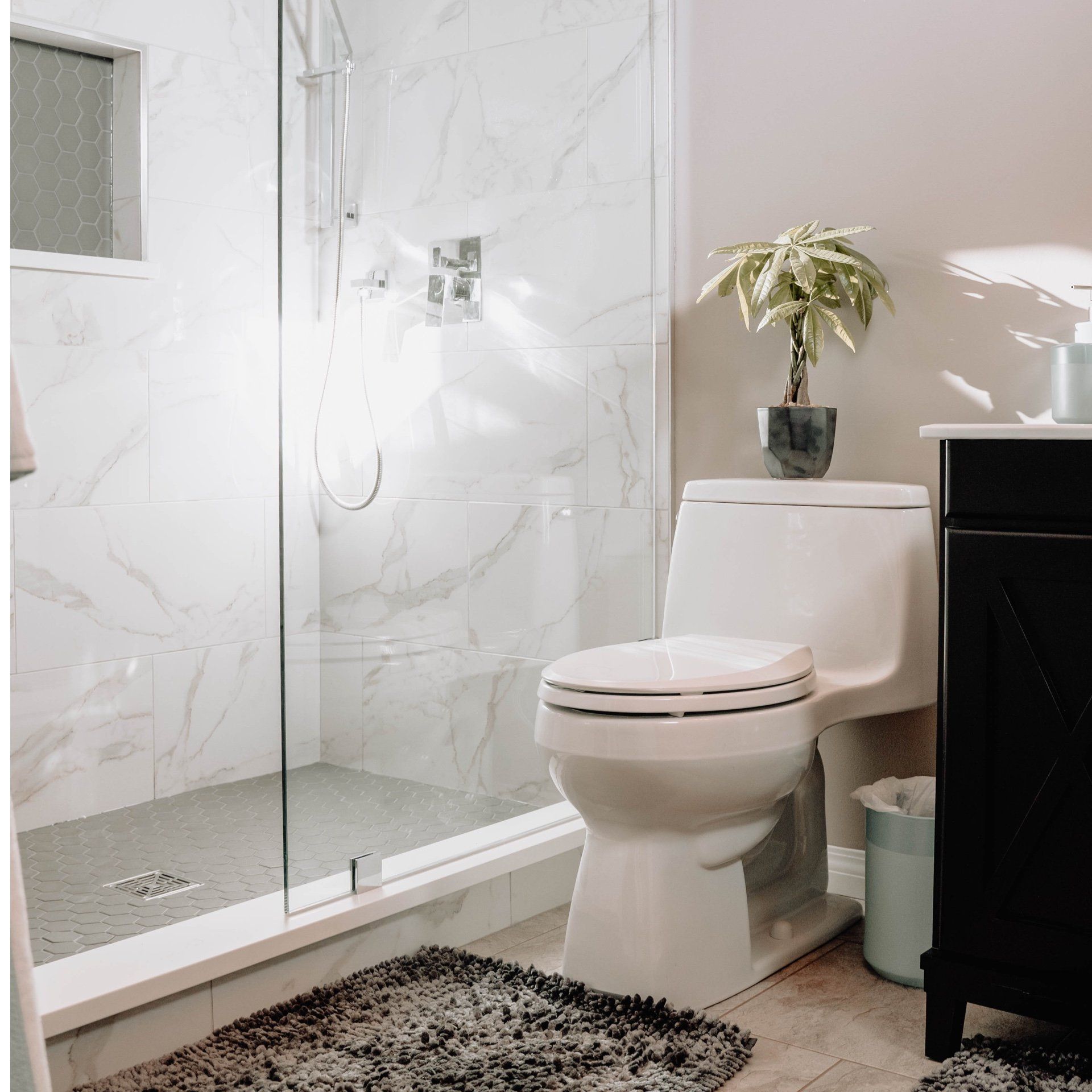 A person installs a large bathroom mirror above a white vanity next to a wooden tiled wall with a towel rack.