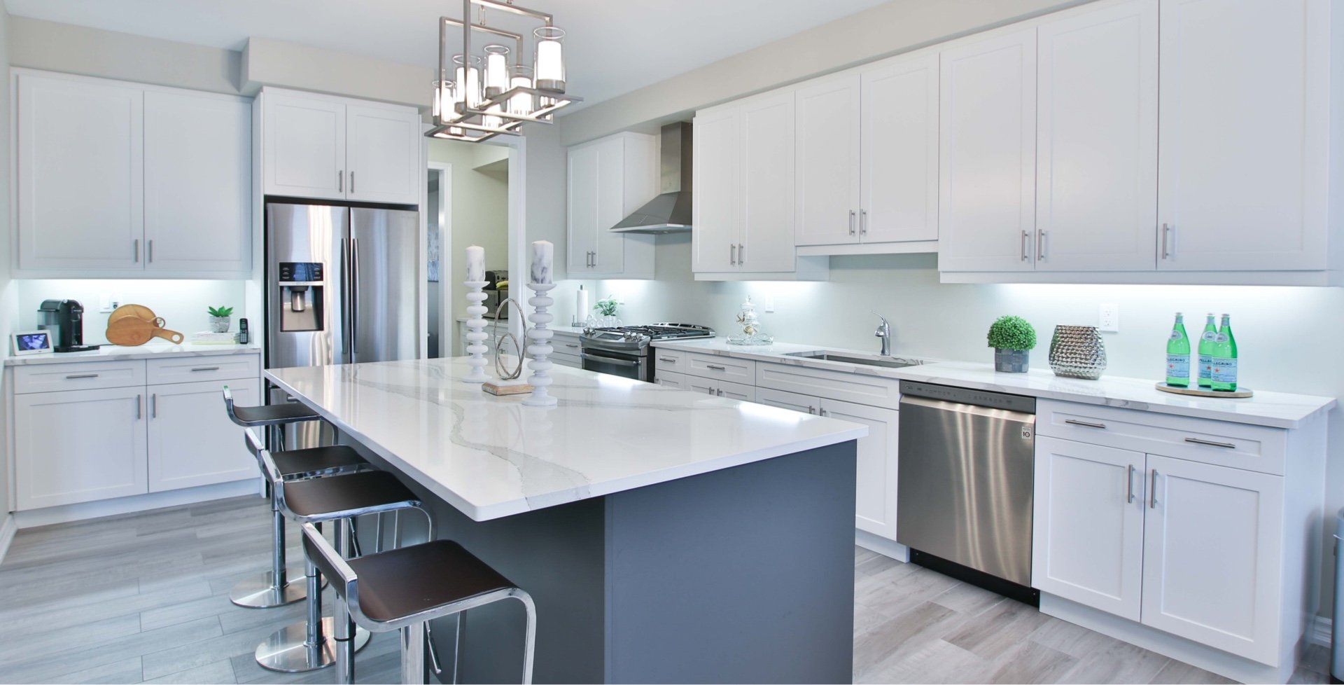 Modern kitchen featuring white cabinets, a large grey island with bar stools, stainless steel appliances, and wood floors.
