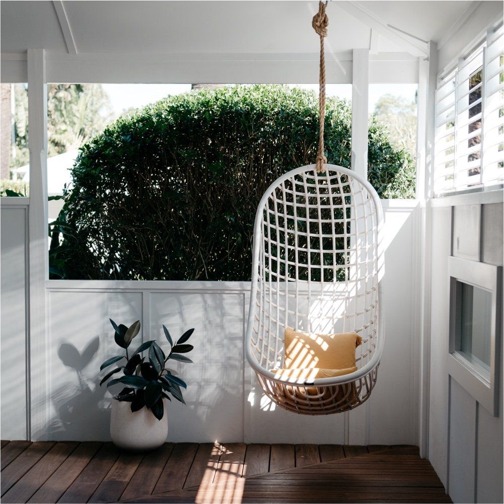 A white hanging chair with a yellow pillow is on a porch.