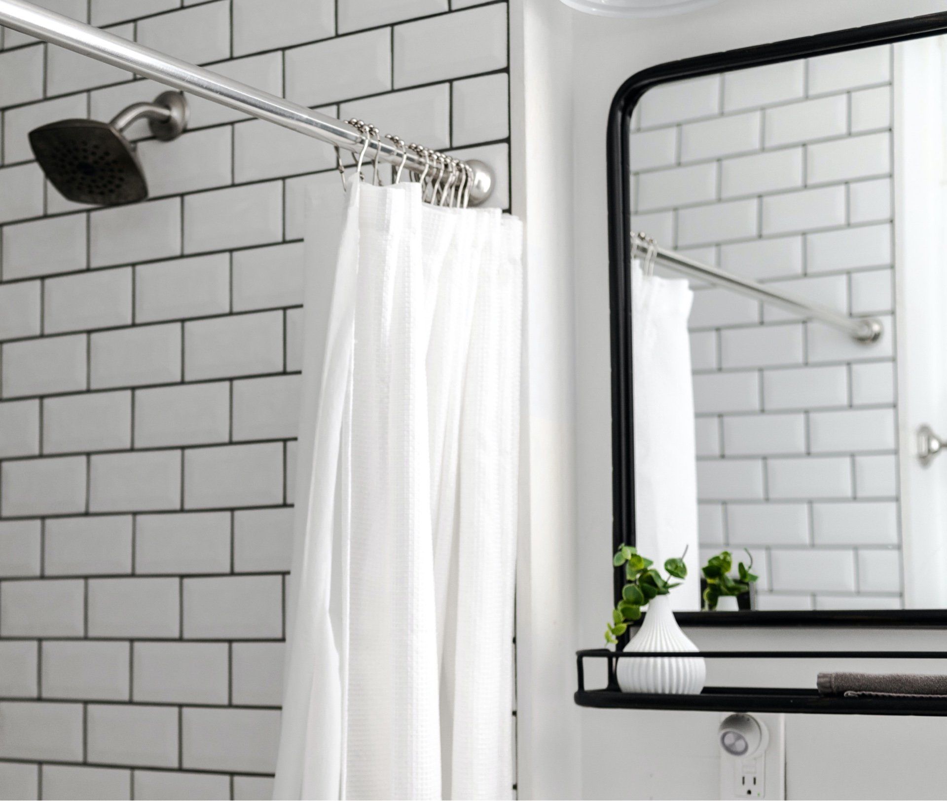 white tiled shower area with black mirror and white shower curtain on a silver rail
