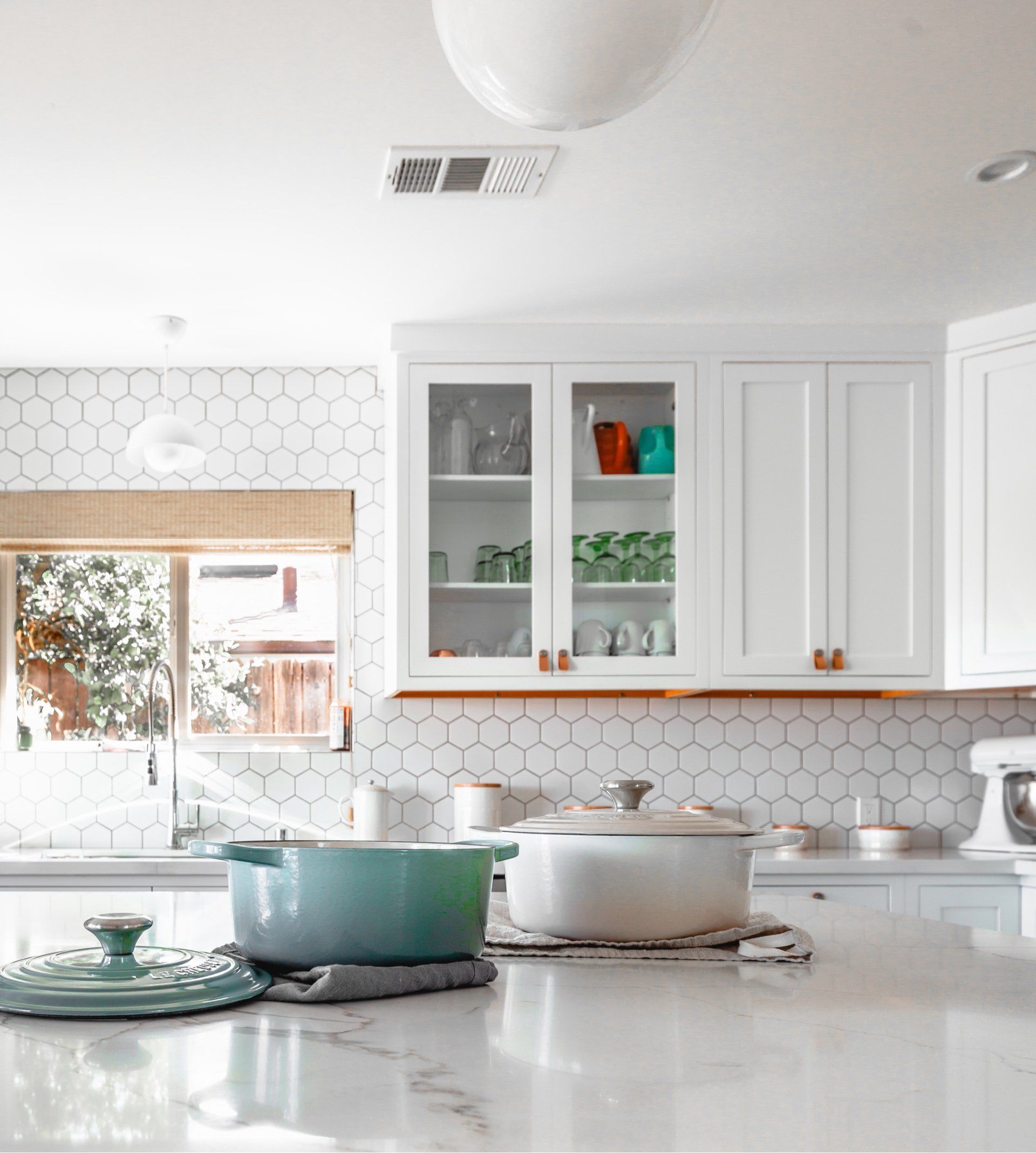 A kitchen with white cabinets , a mixer , pots and pans on the counter.