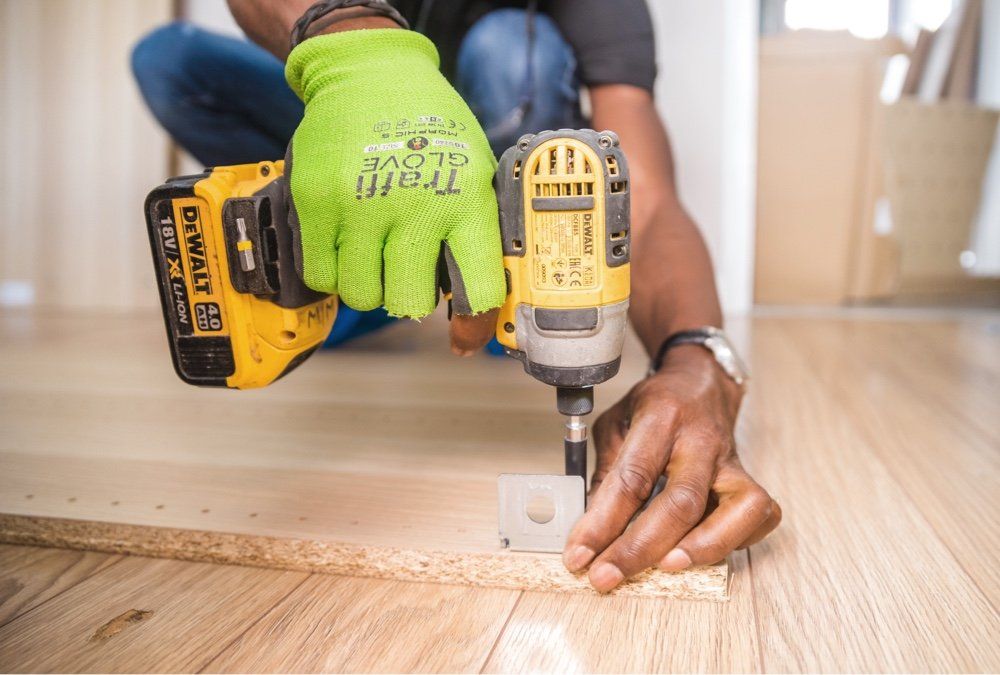 black man in green glove drilling screws into new flooring