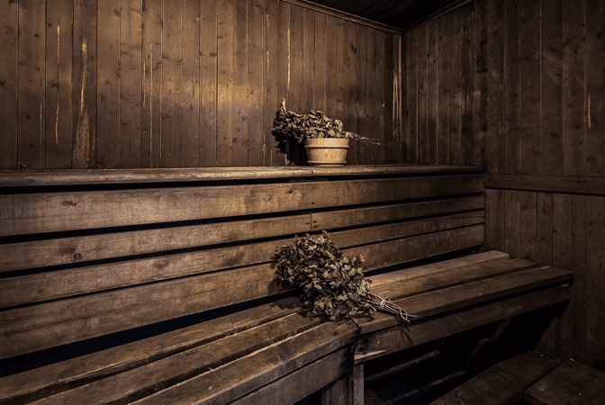A wooden bench in a sauna with a bucket on the shelf.