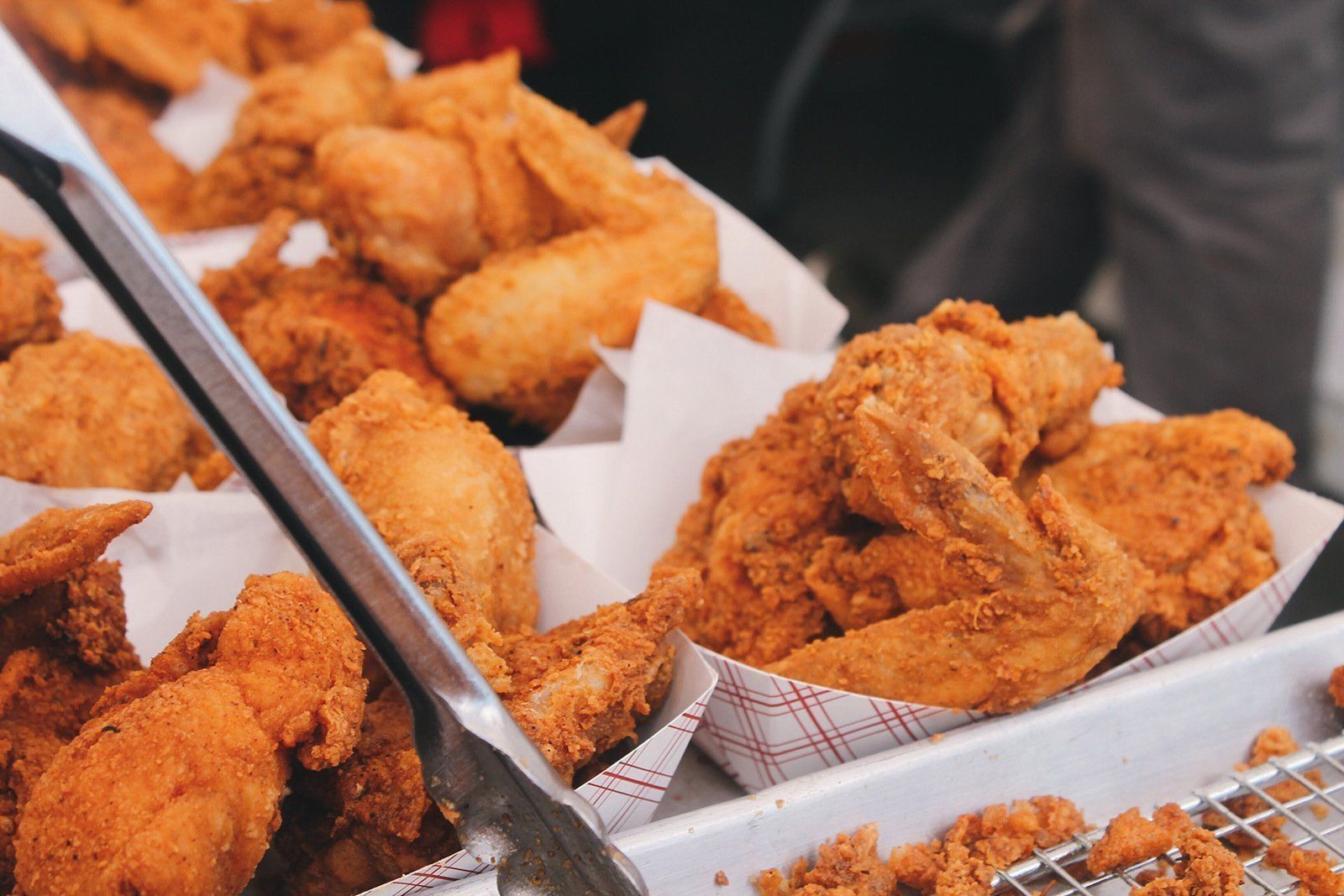 A tray of fried chicken wings and nuggets with tongs.