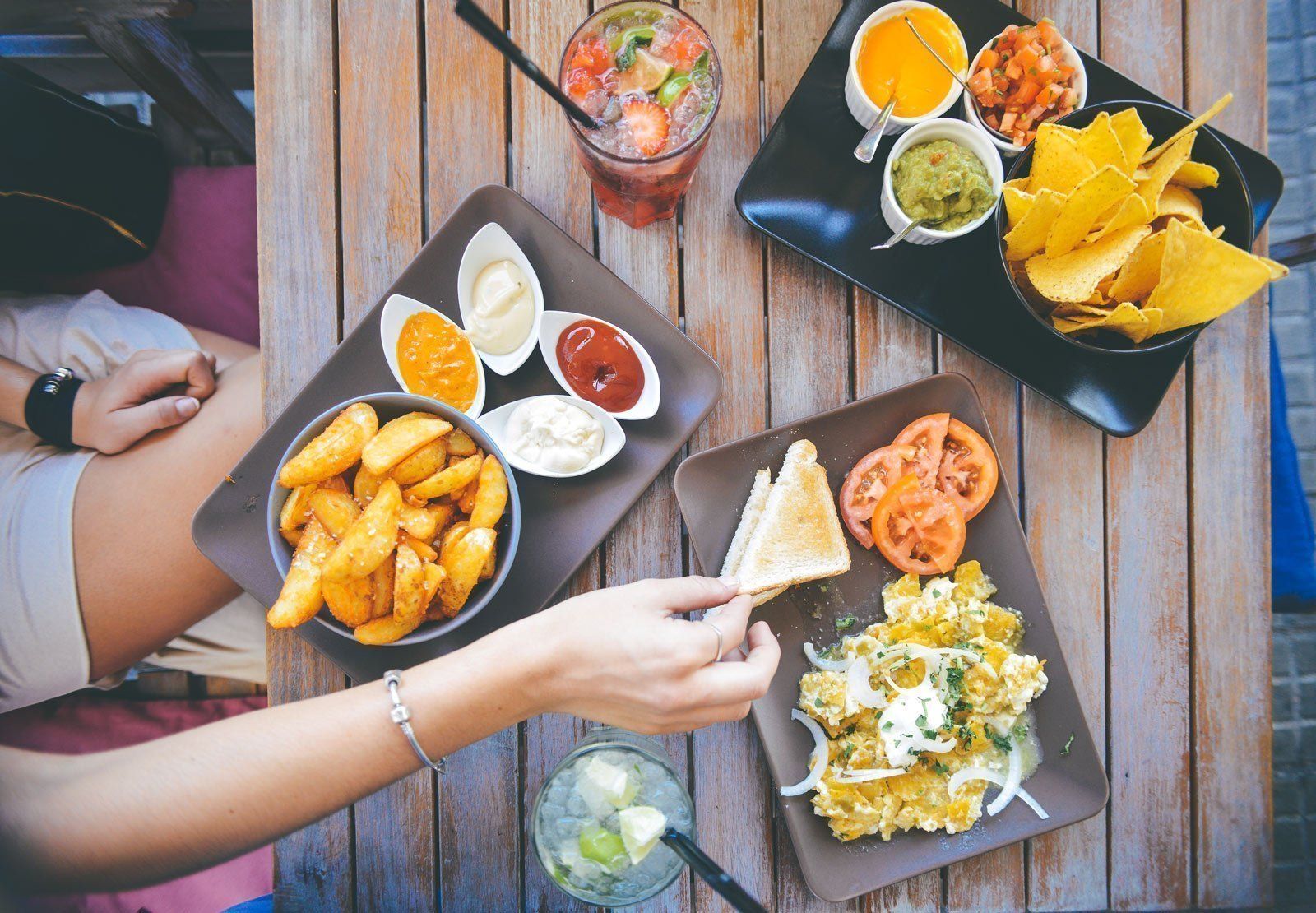 A woman is sitting at a table with plates of food and drinks.