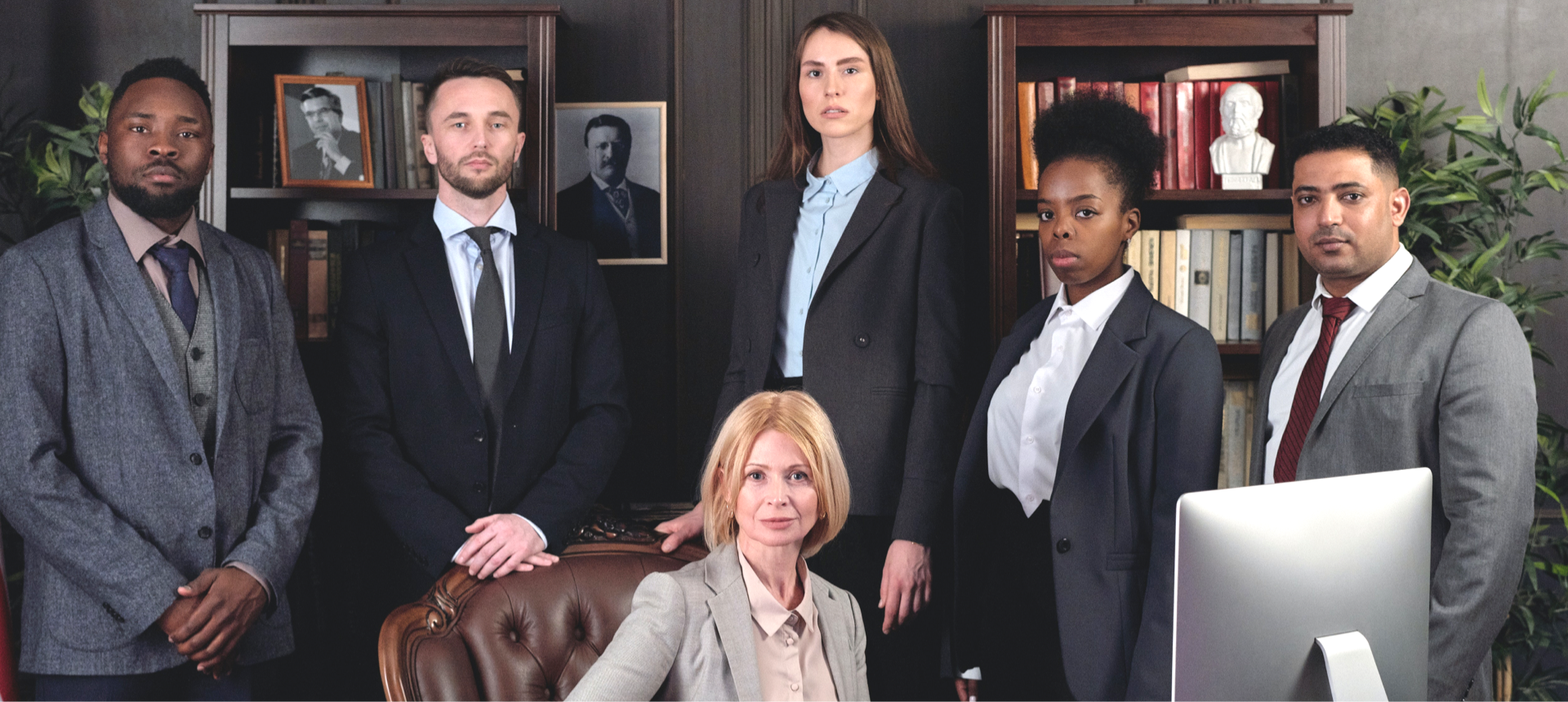 Group of people in suits posing in an office, some standing, some seated.