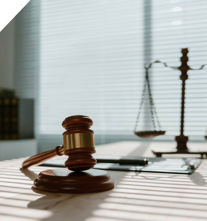 Gavel and scales of justice on a desk by a sunlit window, with papers and a phone nearby