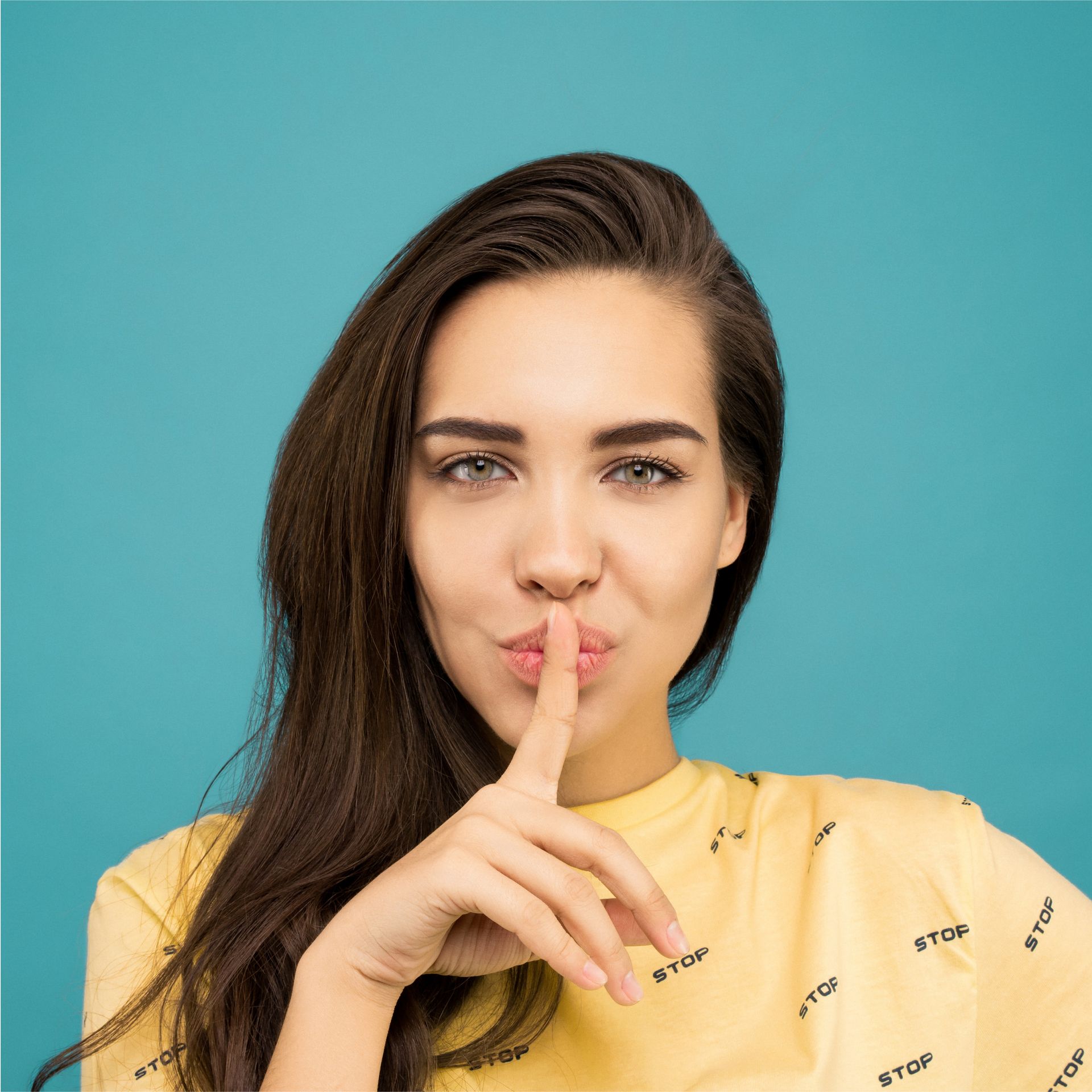 A woman in a yellow shirt is holding her finger to her lips.