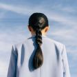 A woman with a braided ponytail is standing in front of a blue sky.