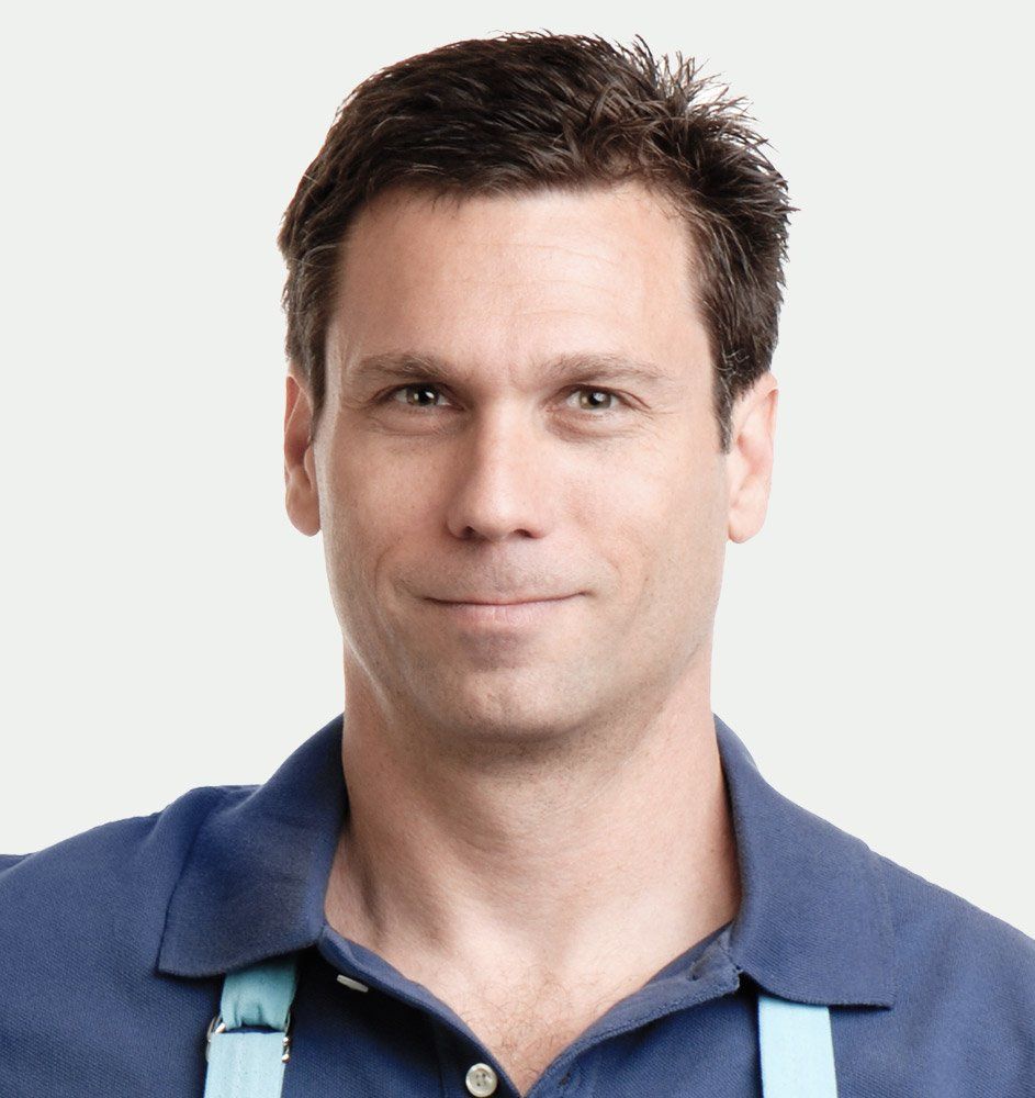 A man wearing a blue shirt and suspenders smiles for the camera