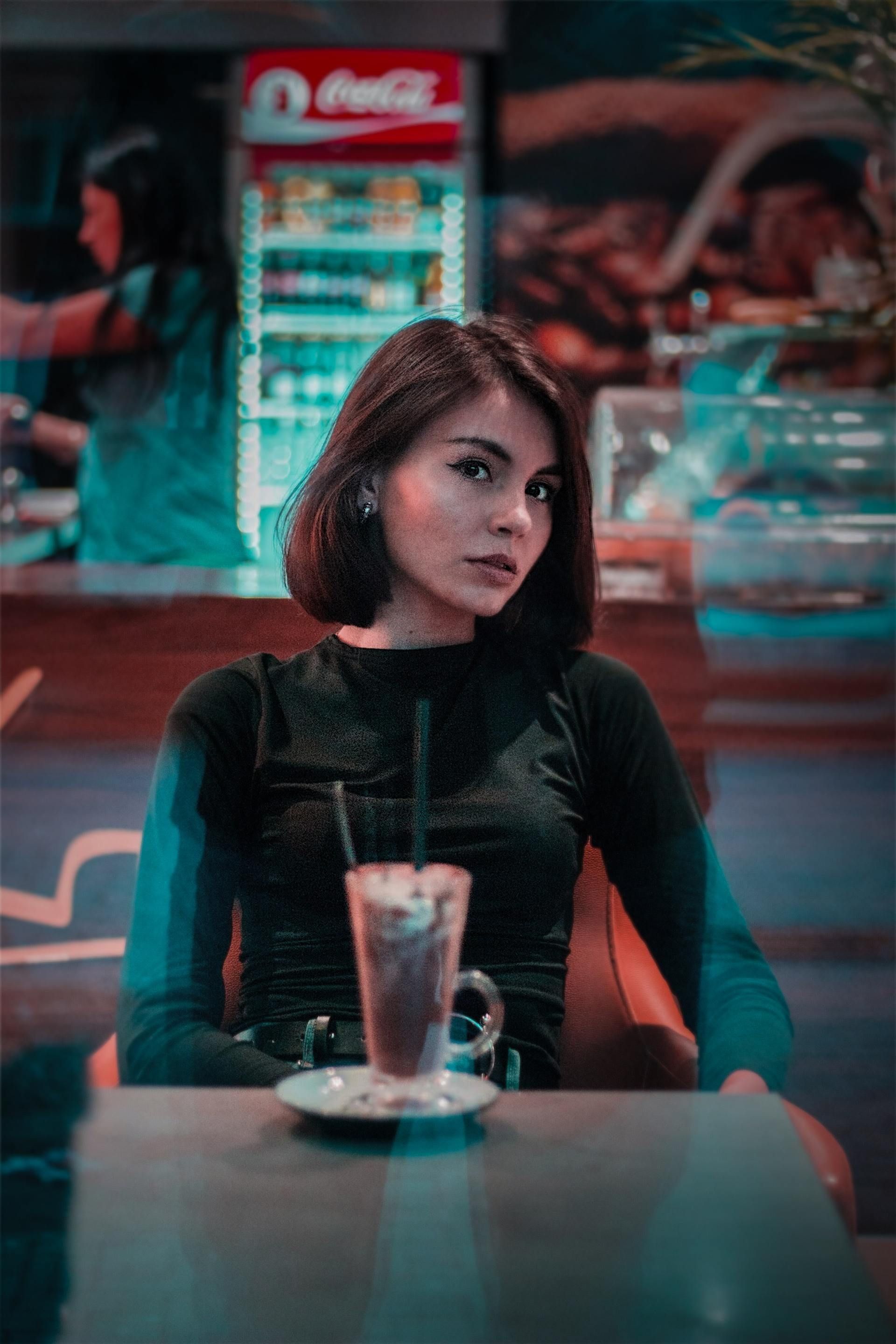 A woman is sitting at a table with a glass of water and a cup of coffee.