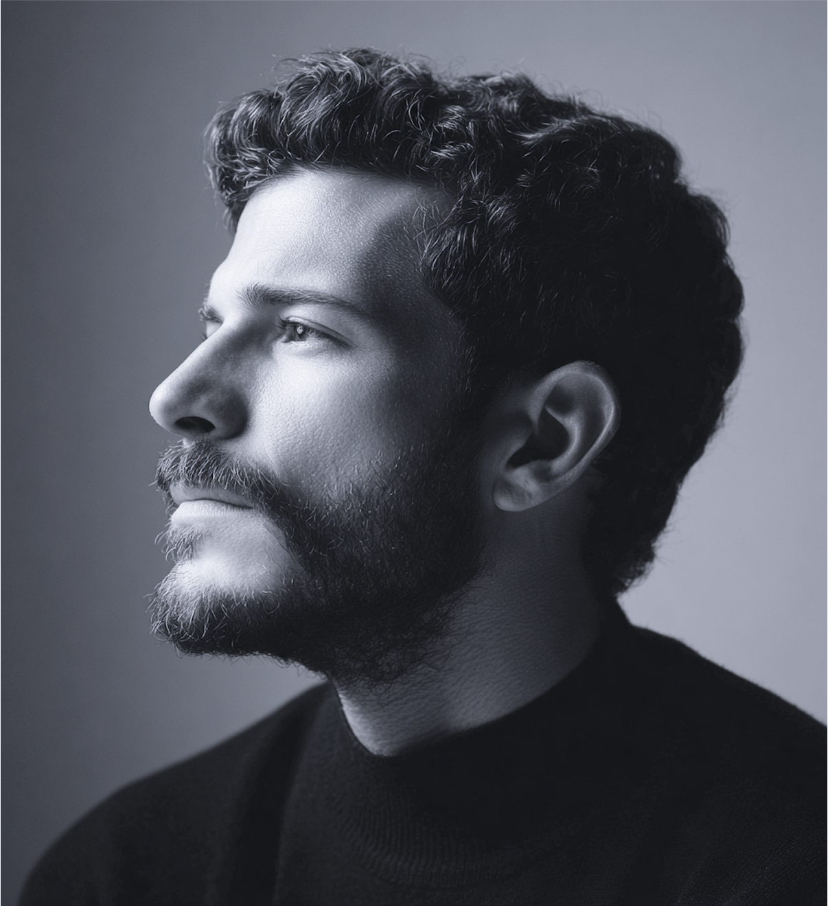 Man with dark curly hair and beard, in profile, looking upwards; black and white.