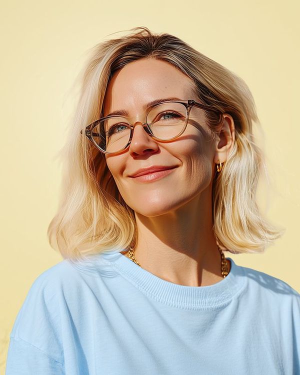 A person wearing glasses and a light blue shirt poses against a solid pale yellow background.