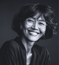 Smiling woman with glasses, dark hair, wearing a dark shirt. Black and white photo.