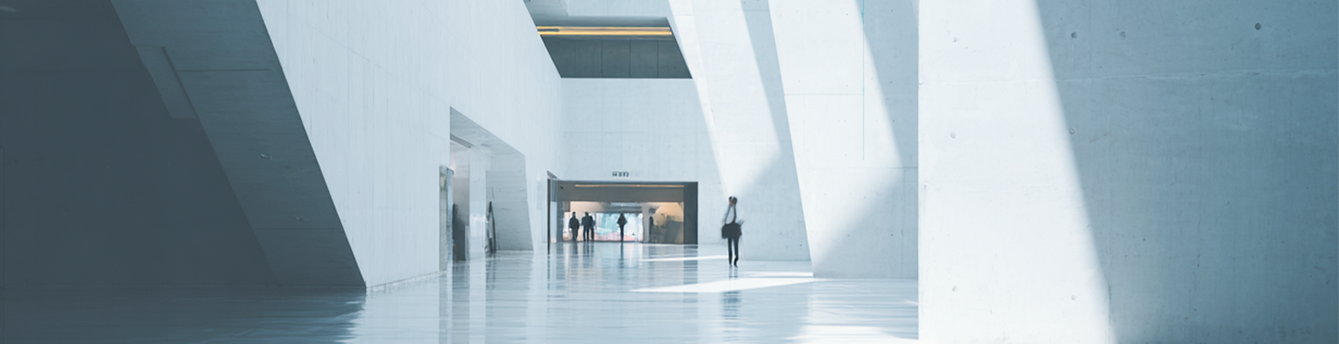 A modern, white interior hallway with a person walking towards the exit.
