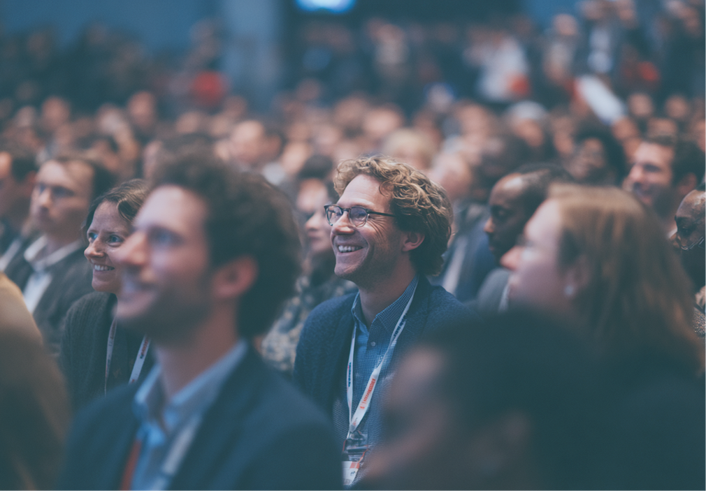 Audience in an auditorium smiling, focused on something ahead.