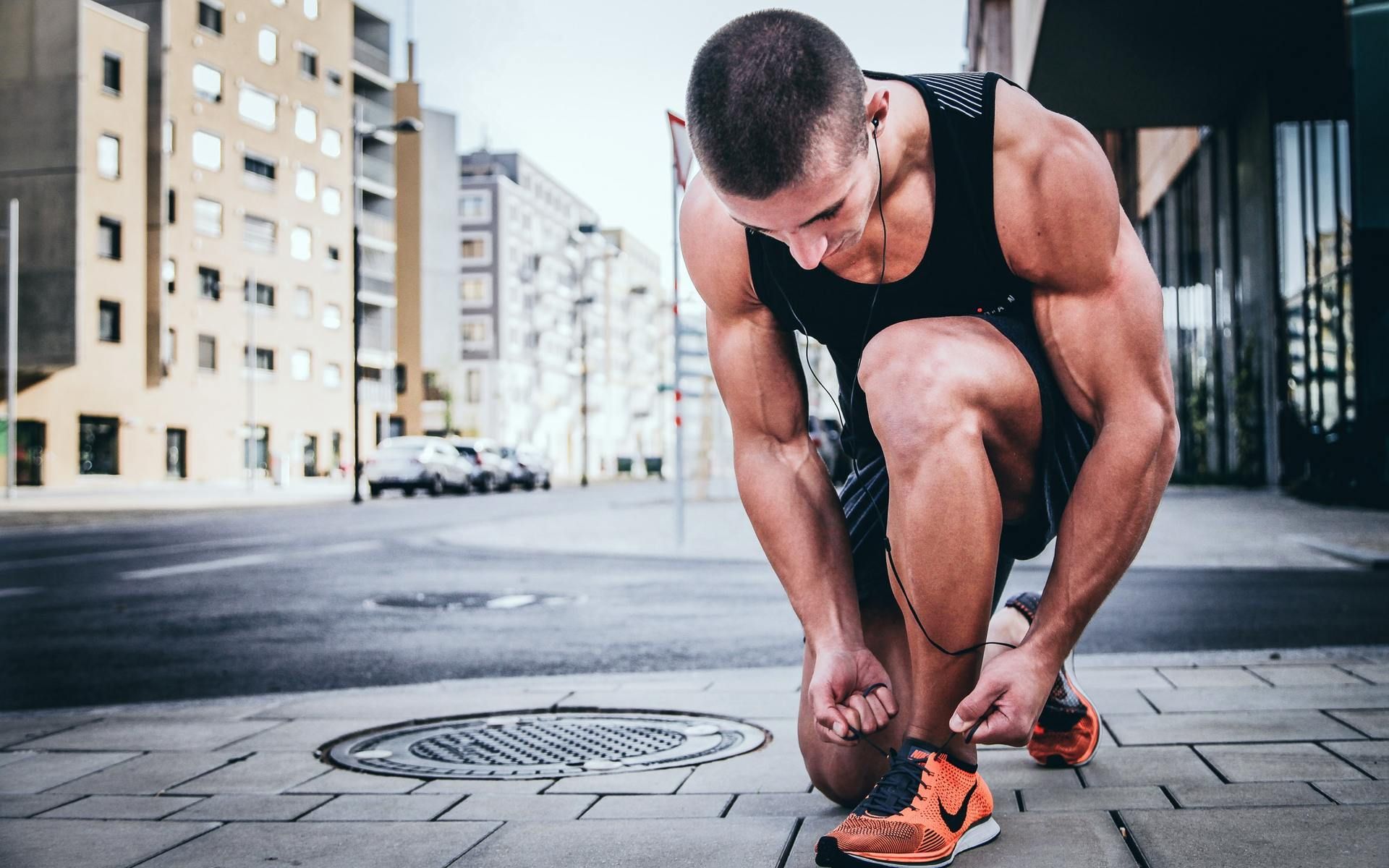 A man is tying his shoes on the sidewalk in a city.