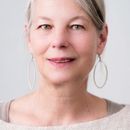 Woman with gray hair and oval earrings, smiling, looking at the camera.