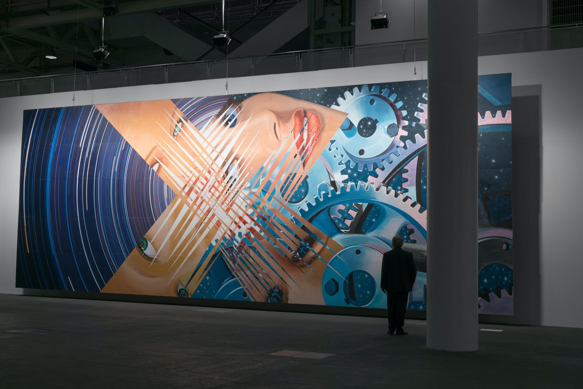 Large abstract artwork with gears, overlapping geometric shapes, and a person viewing it.
