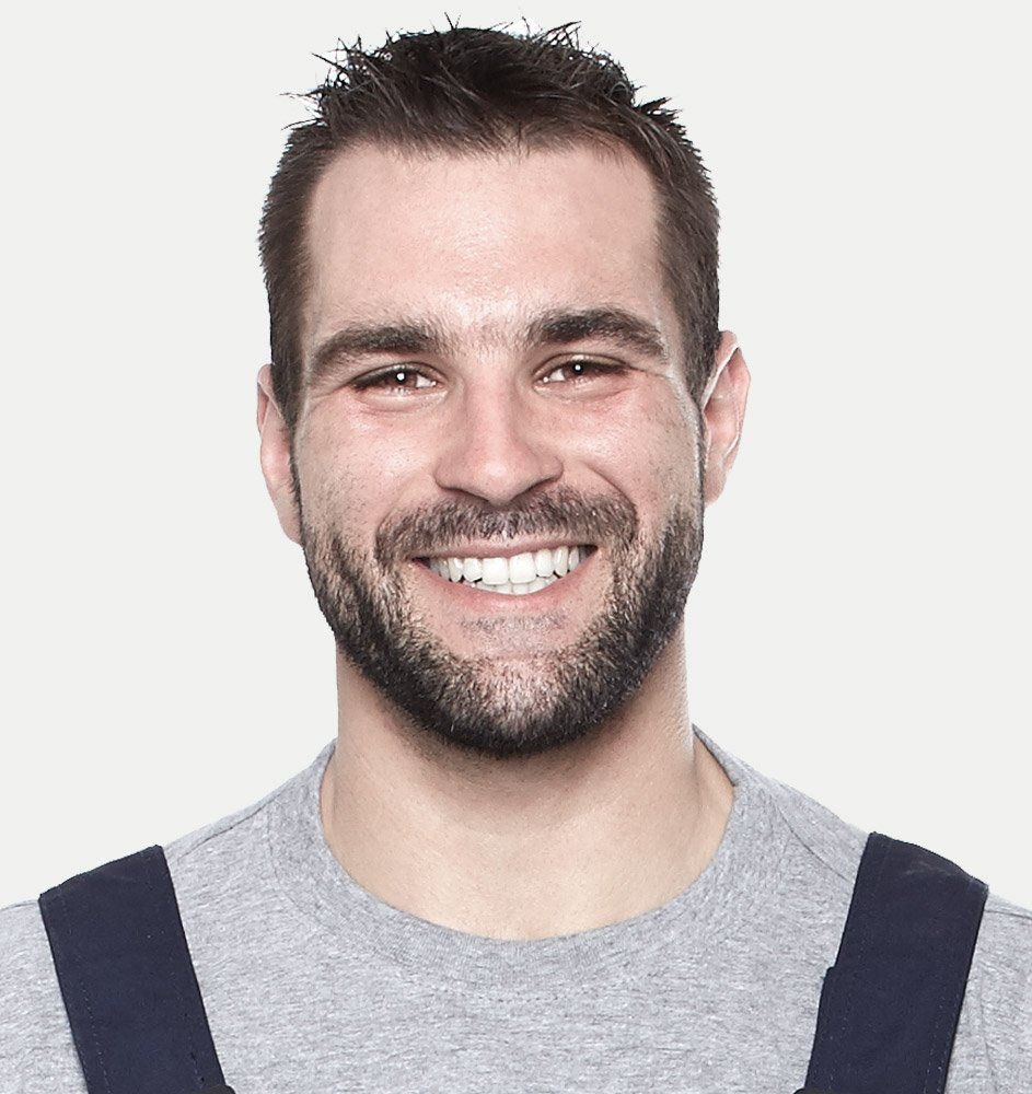 Man with dark hair and beard, smiling broadly, wearing a gray shirt with dark blue straps.