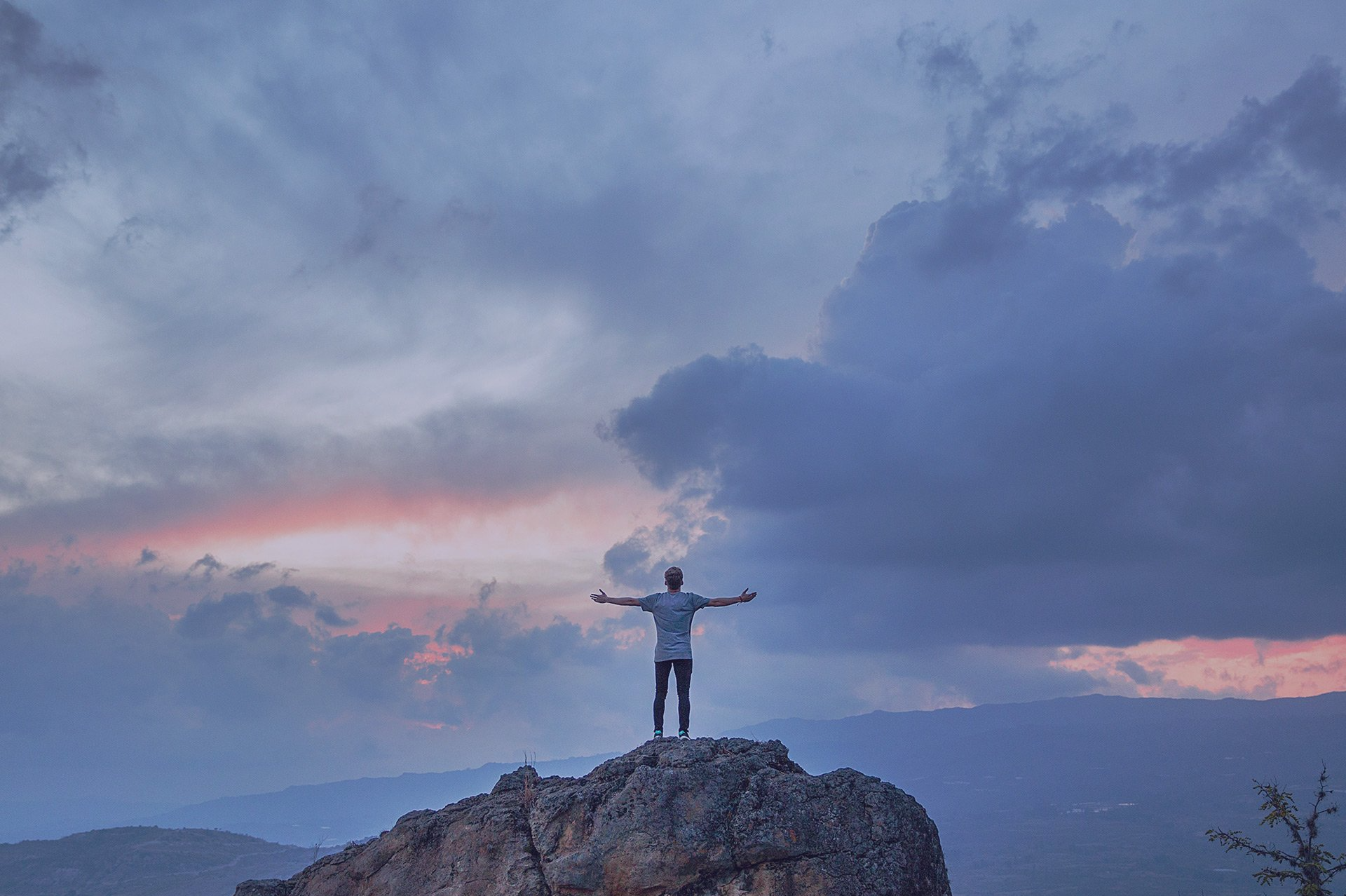 A man is standing on top of a rock with his arms outstretched.