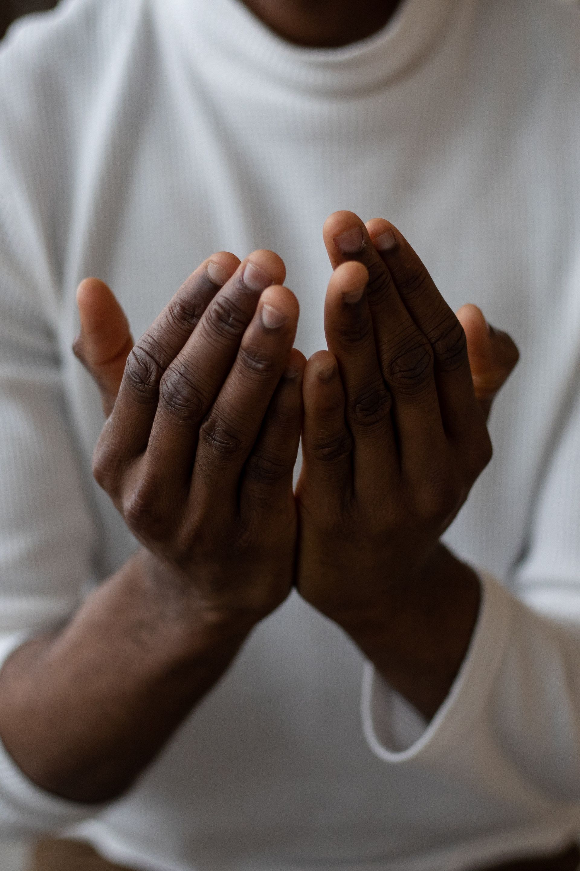 A man in a white sweater is praying with his hands together.