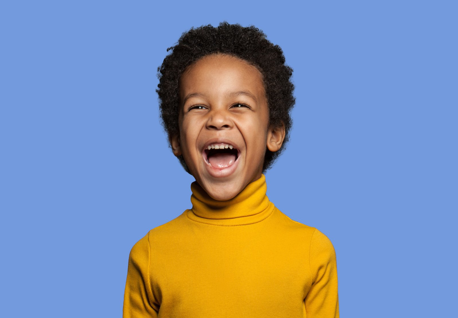 A young boy in a yellow turtleneck is laughing with his mouth open.