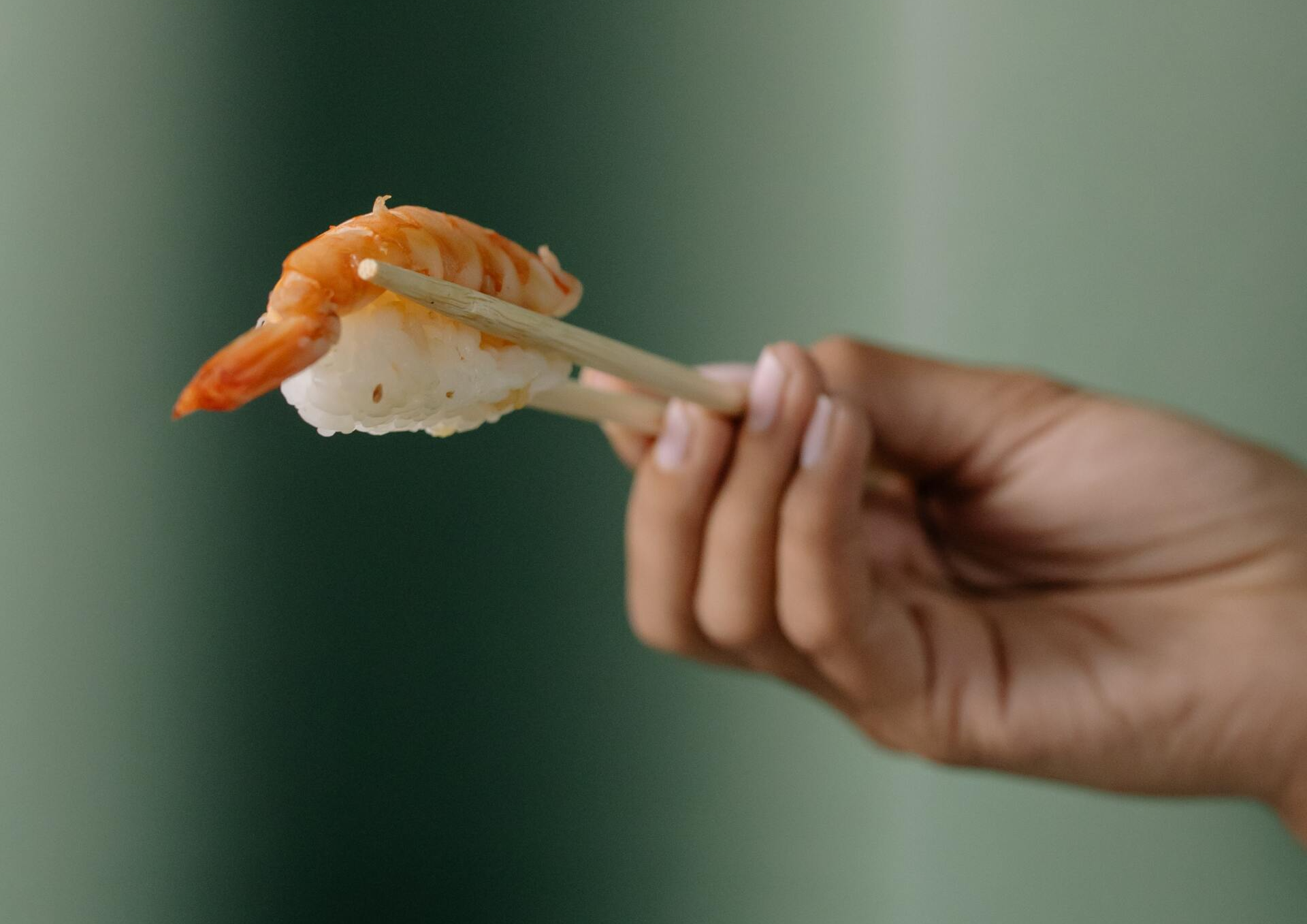 A person is holding a piece of sushi with chopsticks.