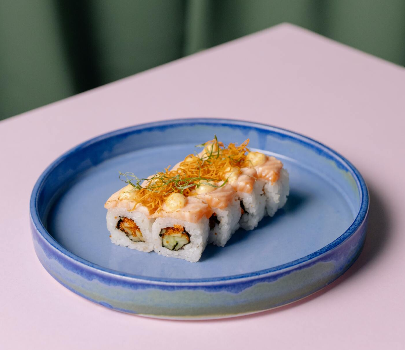 A blue plate topped with sushi on a pink table.
